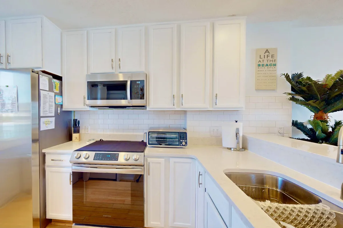 A cheerful kitchen scene showcasing stainless steel appliances, white cabinetry, and beach-themed decor. The space is bright and inviting, clearly designed for cooking, family gatherings, and hosting guests, with a sense of connection to the coastal environment.