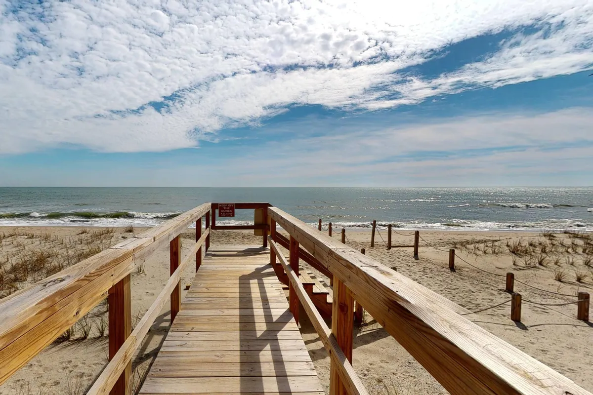 A wooden walkway leading from the property directly to a wide, sandy beach, with an ocean view stretching into the distance. The setting is calm and inviting, promising guests effortless private beach access.